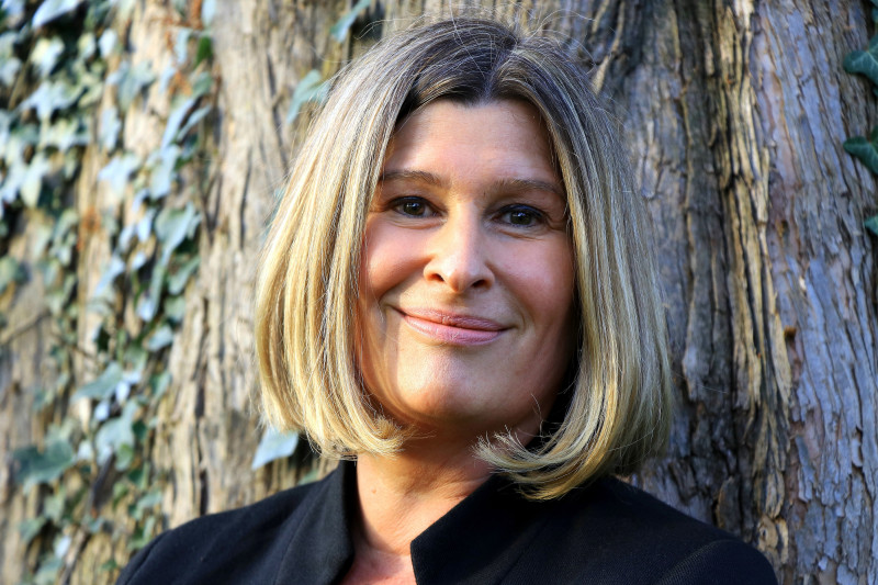 Frau mit blonden Haaren lächelt vor Baum. Porträt.