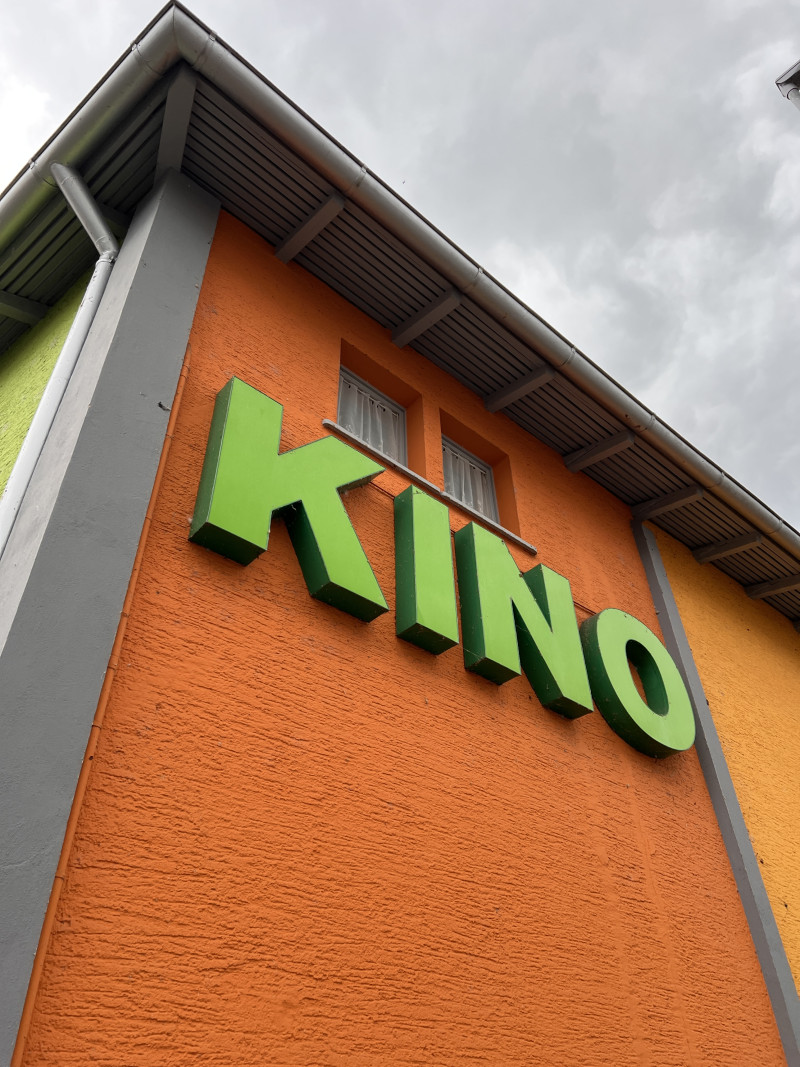 Grünes Kino Schild an orangefarbener Fassade. Architektur eines Kinos.