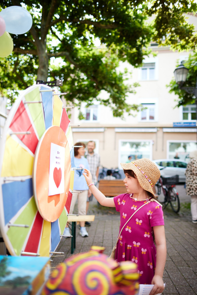 Mädchen dreht am Glücksrad auf einem Strassenfest. Kinderfest mit bunten Farben und fröhlicher Stimmung.