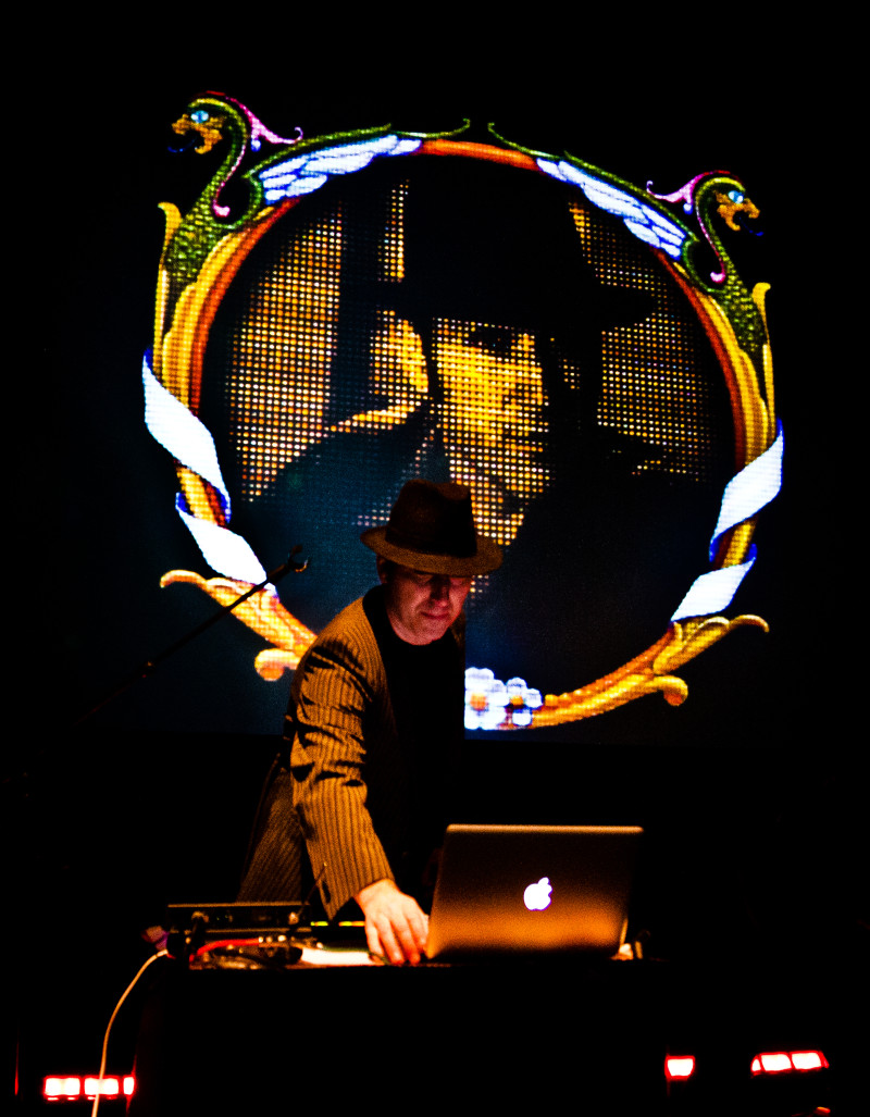 DJ mit Hut und Laptop vor LED-Wand mit Drachen. Musikveranstaltung, Live-Performance, elektronische Musik.