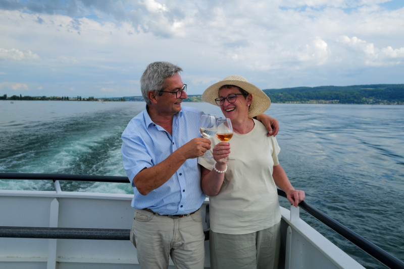 Älteres Paar stößt auf einem Schiff mit Wein an, genießt die Bootsfahrt und den Urlaub.