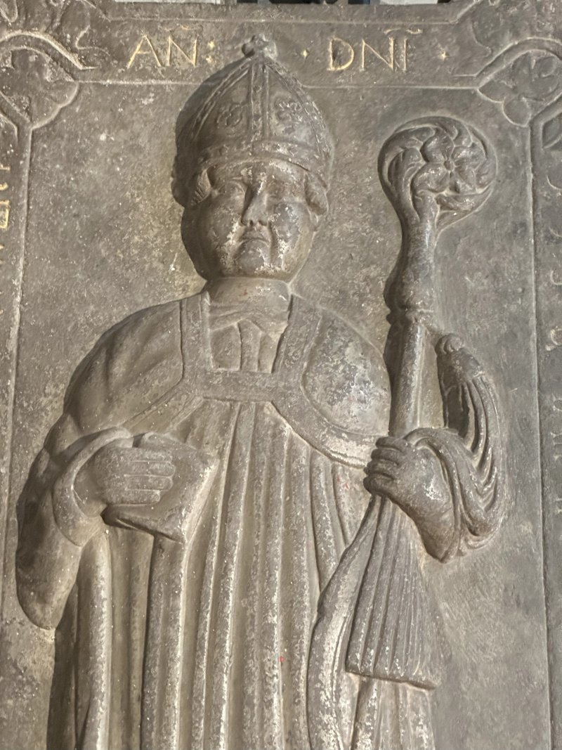 Historische Grabplatte eines Bischofs mit Mitra und Krummstab aus Stein in einer mittelalterlichen Kirche.